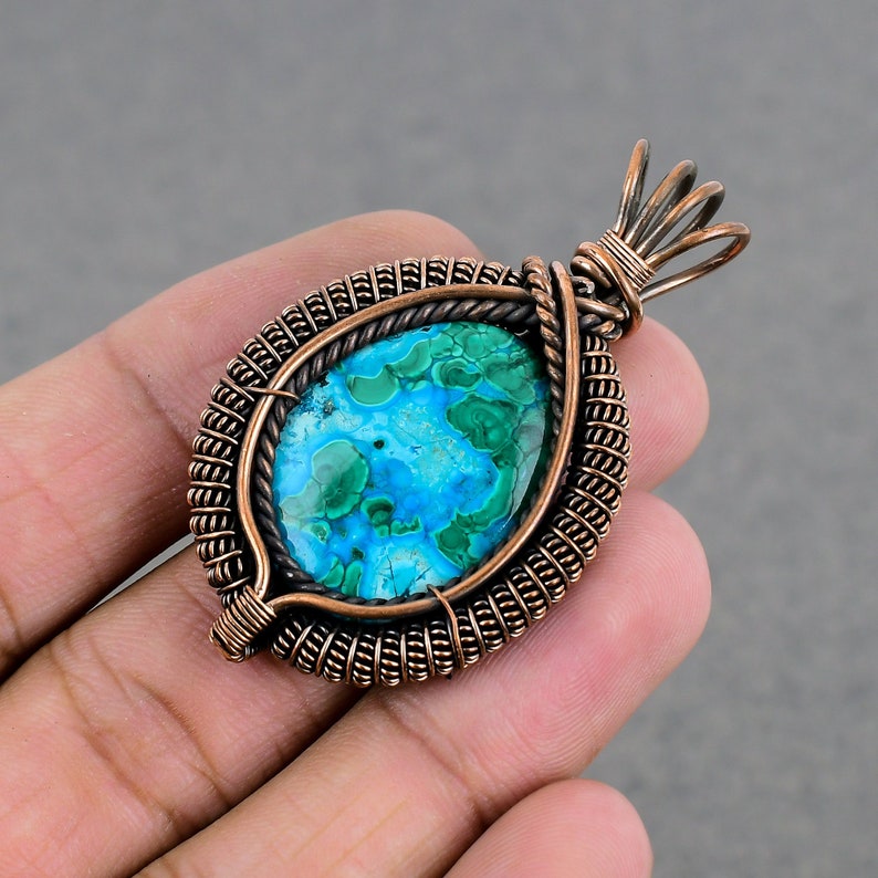 May include: A copper wire wrapped pendant featuring a blue and green gemstone. The pendant has a teardrop shape and is accented with a copper wire bail.