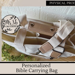 Op de afbeelding: Een witte canvas tote bag met bruine leren accenten en een schouderband. De tas heeft meerdere vakken en is ontworpen om een Bijbel te dragen. De tas heeft een label met de tekst "Ms. Fab Creations".