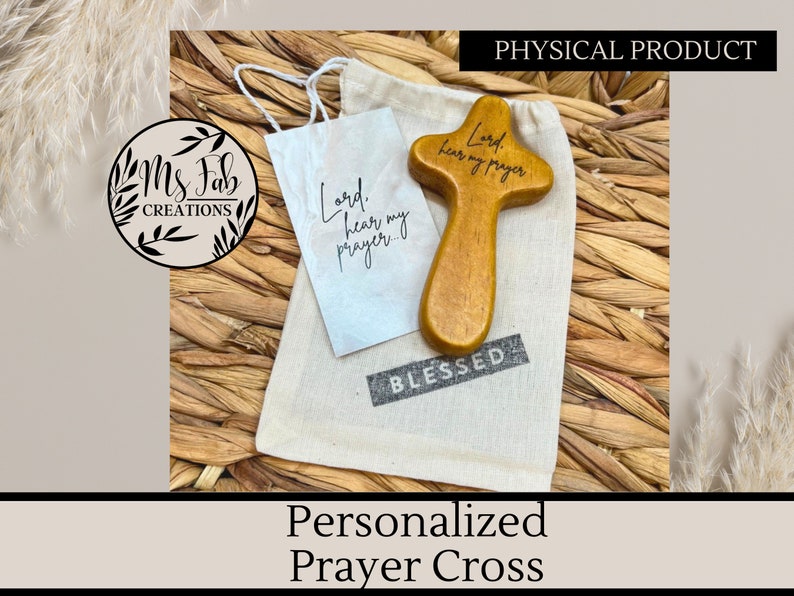 May include: A small wooden prayer cross with the words "Lord, hear my prayer" engraved on it. The cross is sitting on a white cloth bag with the word "BLESSED" printed on it.