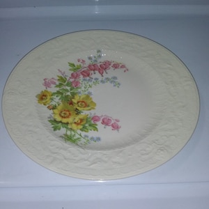 May include: A white ceramic plate with a floral design. The plate features yellow flowers and pink bleeding hearts.