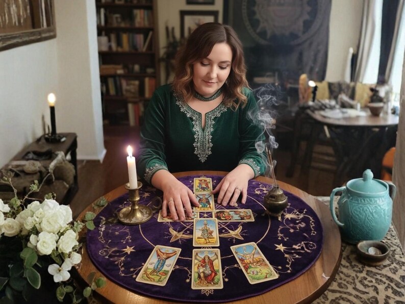 May include: A woman in a green velvet dress is reading tarot cards on a round table. The table is covered with a purple cloth with star designs. A lit candle, incense, and a blue teapot are also on the table.