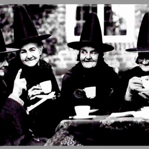 May include: Black and white photograph of four women wearing tall, pointed hats and dark clothing, seated around a table. Each woman holds a teacup and saucer, smiling. The image evokes a vintage, possibly historical, theme.