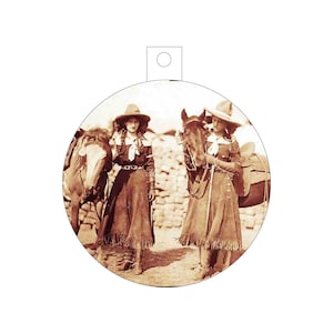 May include: Two women in vintage clothing and wide-brimmed hats stand with their horses. The women are wearing long skirts and boots. The horses are brown and white.
