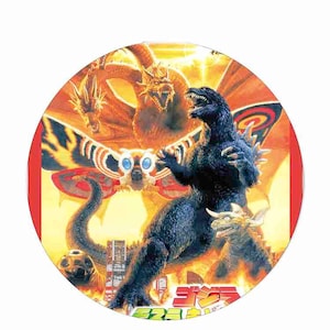 May include: A colorful illustration of Godzilla, Mothra, and King Ghidorah from the Godzilla franchise. The image is set against a fiery orange and yellow background with a cityscape in the foreground. The text "ゴジラ" is visible in the lower right corner of the image.