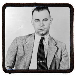 Puede incluir: Una fotografía en blanco y negro de un hombre con traje y corbata. Está mirando directamente a la cámara con una expresión seria. La foto es probablemente una fotografía policial.