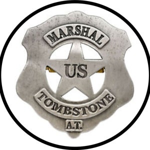 Puede incluir: Una placa de alguacil estadounidense de color plateado con una estrella de cinco puntas y las palabras "MARSHAL US TOMBSTONE A.T."