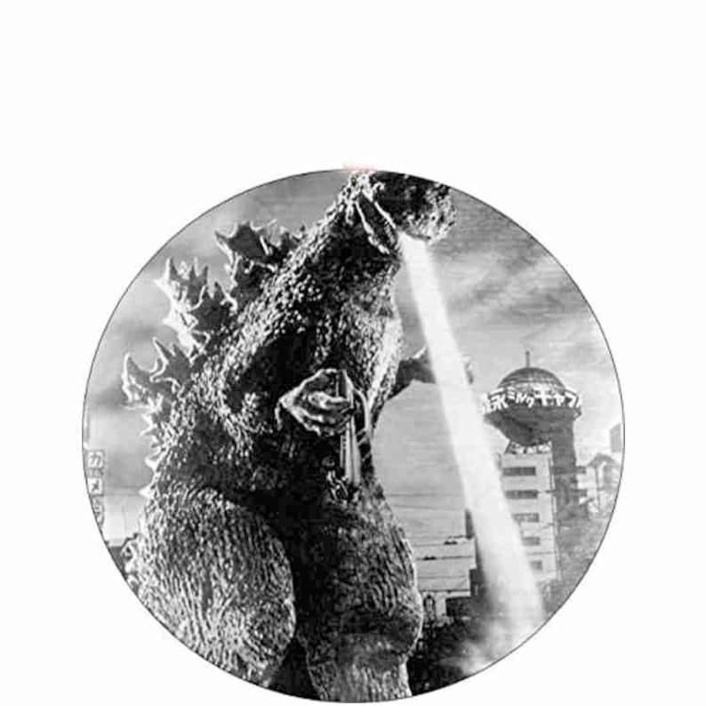 Puede incluir: Imagen circular en blanco y negro de Godzilla, un monstruo gigante, exhalando un rayo de energ&iacute;a. El fondo muestra un paisaje urbano con una torre alta. La imagen es un fotograma de pel&iacute;cula vintage.