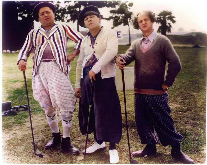 May include: Three men wearing hats and golf attire stand on a green grassy field. The man on the left is wearing a striped jacket, plaid pants, and white socks. The man in the middle is wearing a white sweater, dark pants, and white socks. The man on the right is wearing a brown sweater, plaid pants, and dark socks. All three men are holding golf clubs.