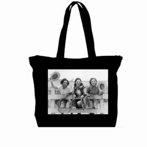 Può includere: Foto in bianco e nero di tre donne che indossano cappelli da cowboy e tengono delle corde. Le donne sono sedute su una recinzione e sorridono. La foto è stampata su una borsa tote nera.
