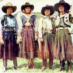 Puede incluir: Cuatro mujeres con sombreros de vaquero y ropa de estilo western. Todas sonríen y miran a la cámara. Las mujeres visten ropa marrón, azul y blanca. Todas llevan botas.