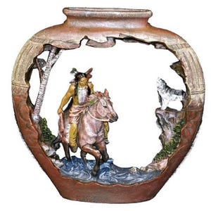 Peut inclure: Un vase décoratif sur le thème amérindien. Le vase présente une scène sculptée d'un Amérindien à cheval traversant une rivière, avec un loup sur une falaise. Le vase est principalement marron avec des accents de vert, de bleu et de blanc.