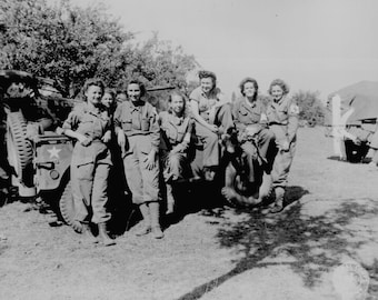 May include: A black and white photograph of a group of women in military uniforms posing with a jeep. The women are standing and sitting on the jeep, smiling at the camera. The jeep has a white star on the side.