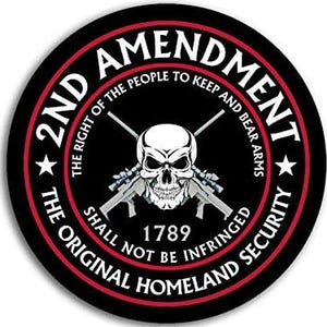 Op de afbeelding: Een zwart en rood rond bord met de tekst "2nd Amendment" in wit. De tekst "The right of the people to keep and bear arms" staat in wit en is om de buitenkant van de cirkel gewikkeld. De tekst "Shall not be infringed" staat in wit en is om de onderkant van de cirkel gewikkeld. De tekst "The original homeland security" staat in wit en is om de onderkant van de cirkel gewikkeld. De tekst "1789" staat in wit en is gecentreerd in de cirkel. Een witte schedel met gekruiste beenderen bevindt zich in het midden van de cirkel.
