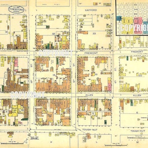 May include: A vintage map of Tombstone, Arizona, showing the location of the gunfight at the OK Corral. The map is printed on a cream-colored paper with brown, yellow, and green lines and text. The map shows the streets and buildings of the town, including the OK Corral, which is marked with an "X".