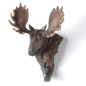 Könnte beinhalten: Ein brauner Elchkopf-Wandhaken mit großen Geweih. Der Haken ist aus Harz und hat einen rustikalen Look.