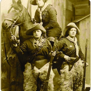 Puede incluir: Fotografía en tonos sepia de tres mujeres vestidas al estilo del Oeste, una de ellas a caballo. Llevan sombreros, chaquetas, pañuelos y chaps. Dos sostienen rifles y todas tienen cinturones de cartuchos, evocando el lejano oeste.