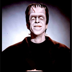 Puede incluir: Un retrato de cerca de un hombre con piel pálida y cabello negro. Lleva una chaqueta marrón oscura y tiene una pequeña cicatriz en la frente. Está sonriendo.