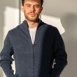 May include: A navy blue zip-up cardigan with a textured knit pattern. The cardigan features a high collar, a full-length zip, and two front pockets. The model is wearing a white t-shirt.