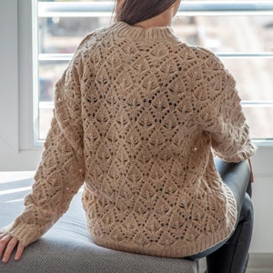 May include: A beige knitted sweater with a delicate openwork pattern.