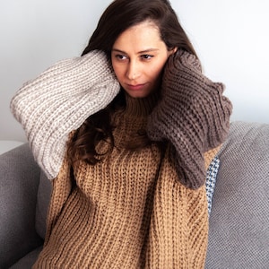 以下が含まれることがあります： 長袖の茶色、ベージュ、グレーのニットセーターを着た女性。セーターはタートルネックで、ざっくりとしたニットの質感です。