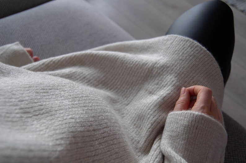 Może przedstawiać: Zbliżenie na osobę ubraną w jasnoszary sweter. Sweter ma żebrowaną fakturę i jest złożony na rękach osoby.
