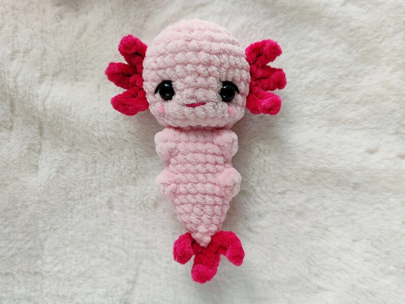 May include: A pink crocheted axolotl plush toy with red fins and black eyes.