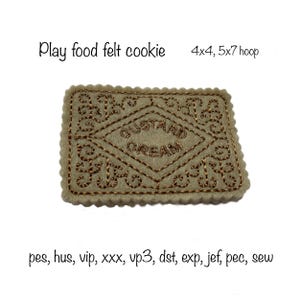 May include: A felt cookie with a brown border and a diamond-shaped center with the words "CUSTARD CREAM" embroidered in brown thread. The cookie is 4x4 inches and is designed for a 5x7 inch embroidery hoop.