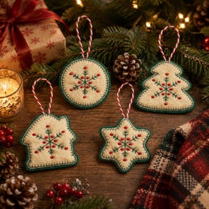 May include: Four felt ornaments in cream with dark green edges and red and green embroidered snowflake patterns. Each ornament features a red and white twisted cord loop for hanging. The shapes include a circle, a tree, a house, and a star.