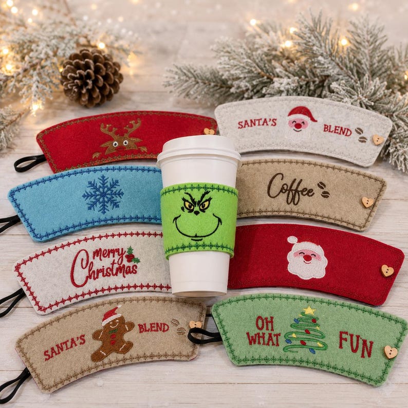 Op de afbeelding: Een collectie vilten koffiebekerhoezen met diverse vakantiemotieven, waaronder een groen Grinch-gezicht, de Kerstman, rendieren, sneeuwvlokken, peperkoekmannetjes en kerstbomen met teksten zoals Santa's Blend en Oh What Fun.