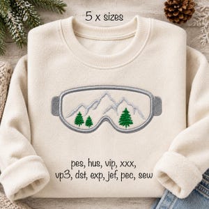 Op de afbeelding: Een crèmekleurig sweatshirt met ronde hals en een borduursel van een skibril met een bergketen en drie groene dennenbomen in de lens. De tekst 5 x sizes en een lijst met bestandsformaten pes, hus, vip, xxx, vp3, dst, exp, jef, pec, sew zijn afgedrukt.