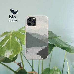 May include: A rectangular phone case with a speckled light gray surface featuring a layered mountain landscape illustration in shades of dark gray and charcoal. The case has a triple camera cutout and the text bio case with a leaf icon above it.