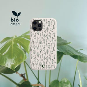 May include: A speckled off-white phone case featuring a dark green botanical pattern of various wildflowers and stems. The case includes a camera cutout and the text bio case with a leaf icon, along with a small U logo at the bottom center.