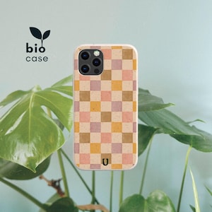 May include: A phone case featuring a checkered pattern in muted shades of pink, yellow, and brown with a speckled texture. The case has a camera cutout and a small logo at the bottom. The text bio case with a leaf icon is visible above.
