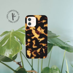 May include: A brown and yellow tortoiseshell phone case with a camera cutout. The case is made from 100% bamboo fiber and is compostable.