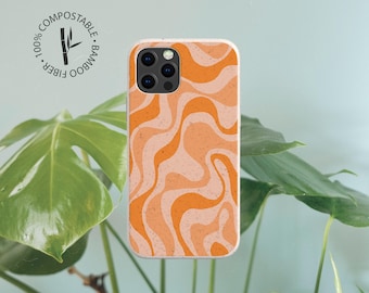 Peut inclure: Une coque de téléphone avec un motif ondulé et marbré dans des tons orange et pêche clair. La coque présente un logo circulaire en haut à gauche avec le texte 100% COMPOSTABLE BAMBOO FIBER et un graphique représentant une tige de bambou.
