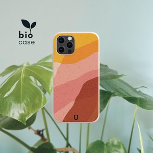 Puede incluir: Una funda para teléfono con un diseño de paisaje abstracto y texturizado con ondas superpuestas de amarillo, melocotón, rosa y naranja terracota. La funda incluye un pequeño logotipo U negro en la parte inferior y el texto bio case con un icono de hoja.