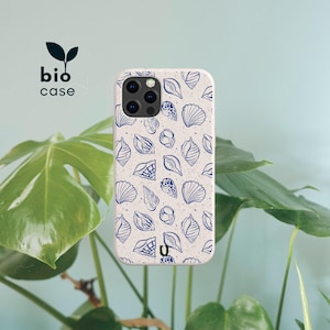 May include: A speckled off-white phone case featuring a repeating pattern of dark blue line-art seashells. The case has a cutout for a multi-lens camera system and includes the text bio case with a small leaf icon printed in the upper left corner.