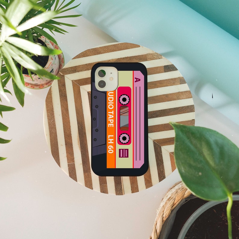 May include: A phone case with a retro cassette tape design. The case is black with a white, orange, and pink cassette tape design. The text on the case reads "Audio Tape LH 60".