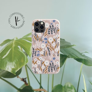 May include: A rectangular phone case with a light pink background featuring a repeating pattern of white flowers, dark green leafy stems, and mustard yellow foliage. A circular logo in the top left corner reads 100% COMPOSTABLE BAMBOO FIBER.