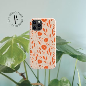 May include: A phone case with a cream-colored background and a repeating pattern of orange leaves and stems. The case features a circular logo in the top left corner with the text 100% COMPOSTABLE BAMBOO FIBER and a bamboo stalk icon.