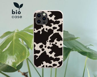 Peut inclure: Une coque de smartphone rectangulaire avec un motif de taches de vache noir et blanc. La coque présente une découpe pour un système de caméra à trois objectifs. Le texte bio case est imprimé en noir avec une petite icône de feuille au-dessus.