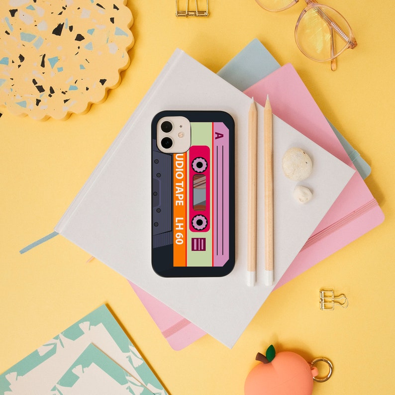 May include: A black phone case with a colorful cassette tape design. The case features the text "AUDIO TAPE LH 60" and the letter "A" on the cassette tape.