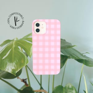 May include: A pink and white gingham patterned phone case with a dual camera cutout. A circular logo in the upper left corner features a bamboo stalk graphic and the text 100% COMPOSTABLE BAMBOO FIBER.