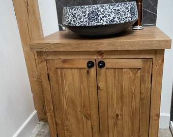 Op de afbeelding: Een houten kast met twee deuren en een witte keramische wastafel met een blauw en zwart bloemenmotief. De wastafel staat op de kast en er is een koperen kraan met een witte hendel.