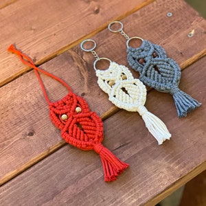 May include: Three macrame owl keychains with wooden beads. The owls are in red, white, and gray.