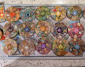 May include: A collection of colorful spinning tops featuring various Pokémon characters and designs. The tops are arranged on a gray mat, with several packs of Pokémon cards visible in the upper left corner. The tops have a diameter of approximately 3 inches.