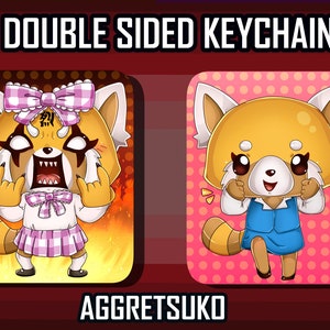May include: Double-sided keychain featuring a cartoon red panda character. One side shows the character with a pink bow and a fierce expression, while the other side shows the character with a happy expression and a blue dress. The text "AGGRESUKO" is printed below the keychain.