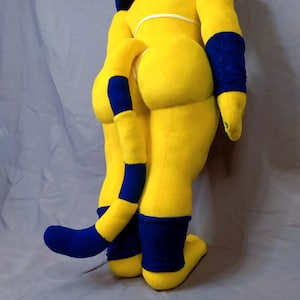 Puede incluir: Un juguete de peluche amarillo con una cola a rayas azul y amarilla, pu&ntilde;os azules y un cuerpo amarillo. El juguete est&aacute; posado con las piernas dobladas y la cola enroscada alrededor de su cuerpo.