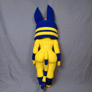 Puede incluir: Un juguete de peluche con forma de gato con una cabeza a rayas azules y amarillas y un cuerpo amarillo. El juguete lleva un atuendo a rayas azules y amarillas y tiene una cola larga.