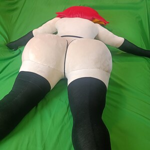 Puede incluir: Una mu&ntilde;eca de peluche en posici&oacute;n supina, con torso blanco, medias negras y un gorro rojo. Los brazos de la mu&ntilde;eca est&aacute;n extendidos y las piernas separadas. El fondo es verde liso.